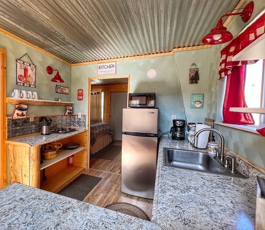 A compact kitchen with a refrigerator, microwave, sink, and wooden shelves.