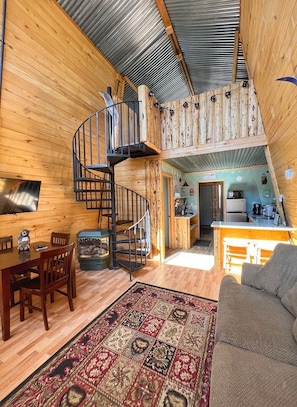 Interior acogedor de una cabaña con detalles de madera, una escalera espiral, un comedor y una cocina.