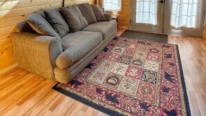 Ein gemütliches Zimmer mit schrägverkleidetem Holzboden, einer Couch, einem gemusterten Teppich und einer Lampe.