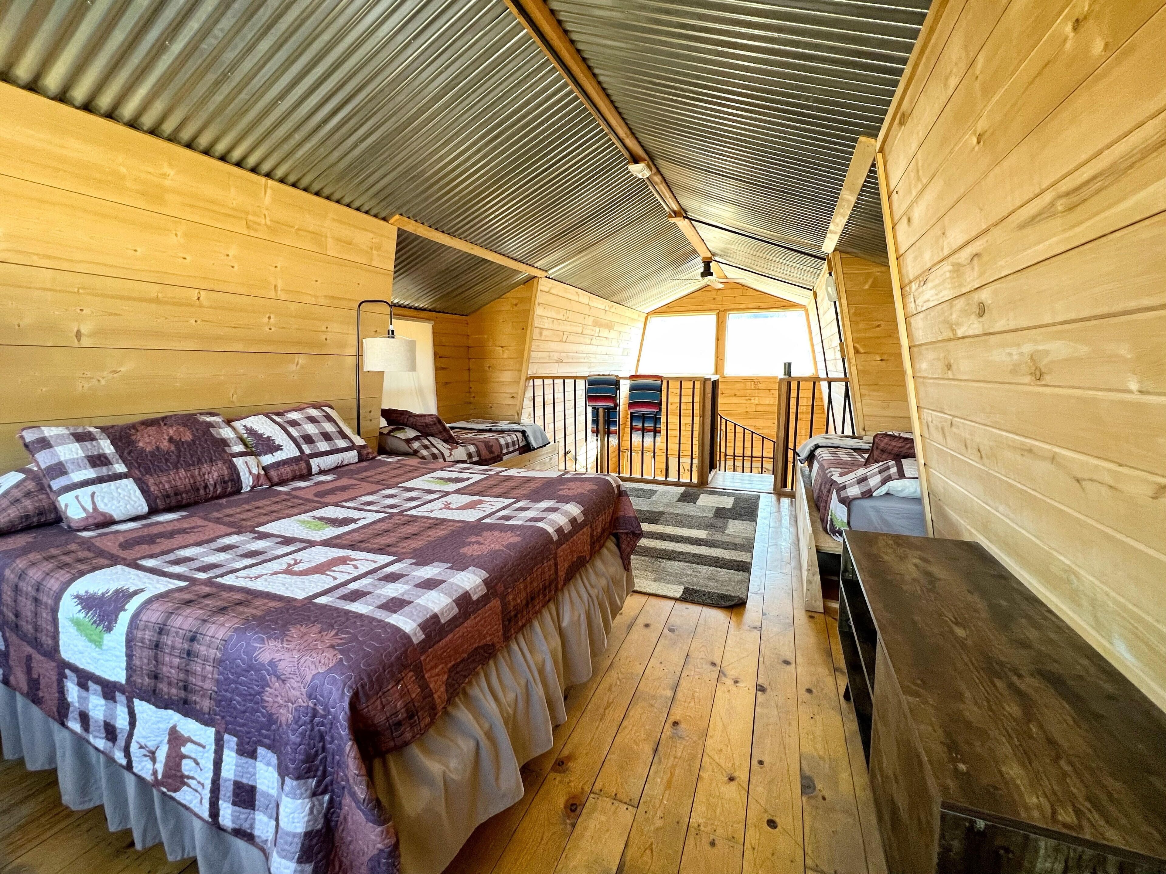 Une cabane confortable avec un grand lit, un bureau et un escalier menant à une mezzanine.