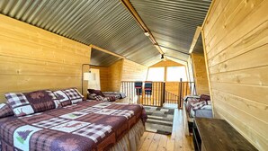 Een gezellig vakantiehuisje met een groot bed, een bureau en een trap naar een zolderruimte.