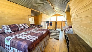 Une cabane confortable avec un grand lit, un bureau et un escalier menant à une mezzanine.