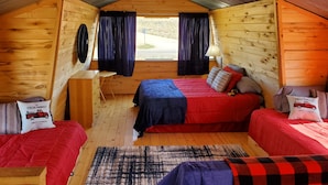 Una cabaña con dos camas, un escritorio pequeño y una ventana con cortinas.