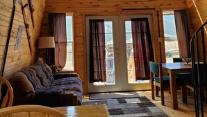 Interior acogedor de una cabaña de madera con habitación en el entrepiso, comedor y vistas al exterior.