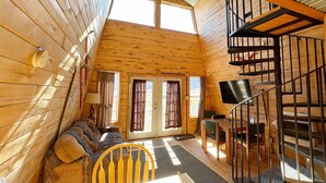 Una cabaña acogedora con un altillo que funciona como dormitorio, una zona de comedor y una escalera.