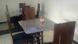 A dining area with a table and chairs, a television mounted on the wall, and two wall-mounted lamps. - Le Grand Hotel Oyugis (Oyugis)