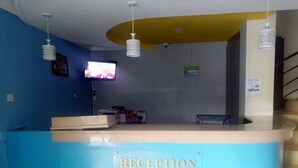 A reception area with a blue counter, a television mounted on the wall, and a sign indicating a smoking area. - Le Grand Hotel Oyugis (Oyugis)