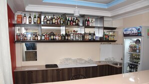 A bar area with shelves stocked with various liquor bottles, a refrigerator with beverages, and a counter with glasses and a phone. - Le Grand Hotel Oyugis (Oyugis)
