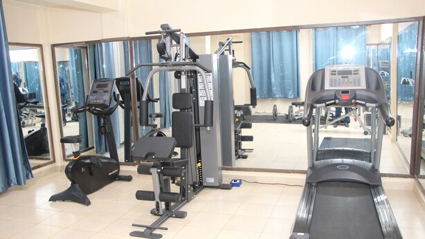 A gym with exercise equipment, including a treadmill, weight machines, and a mirror wall. - Le Grand Hotel Oyugis (Oyugis)
