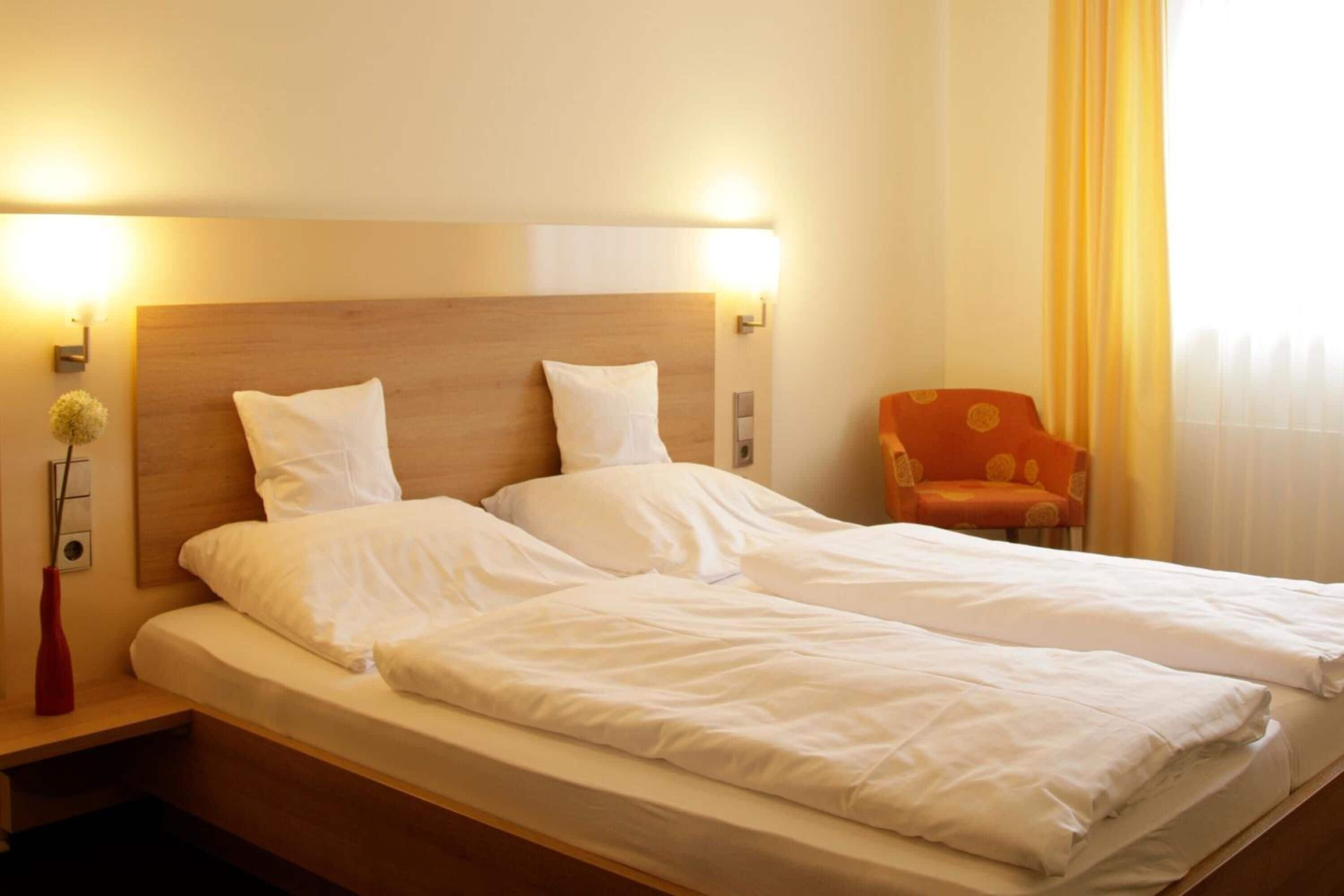 A double bed with white linens, a wooden headboard, and two wall-mounted light fixtures.