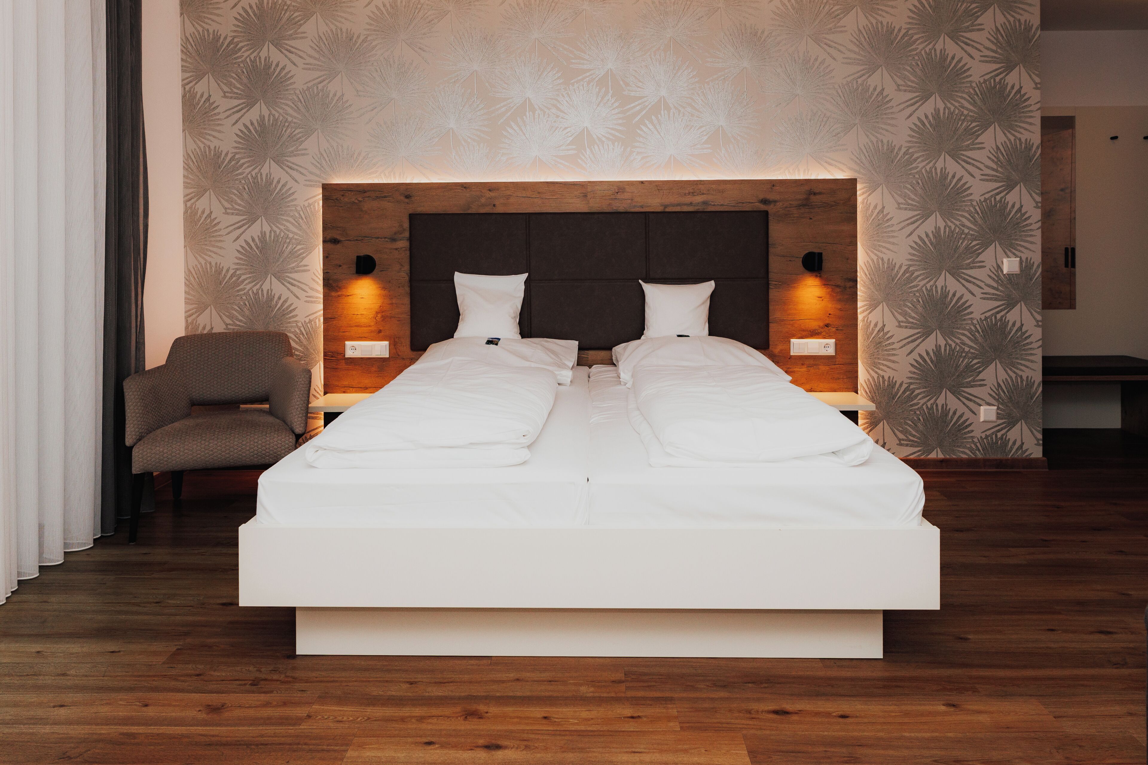 Une chambre à coucher moderne avec un grand lit, une tête de lit en bois et un papier peint à motifs.