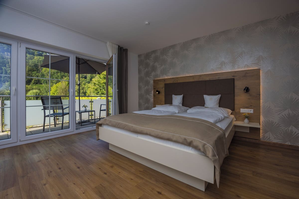 A bedroom with a large bed, a wooden headboard, a nightstand, and a sliding glass door leading to an outdoor area with a table and chairs.