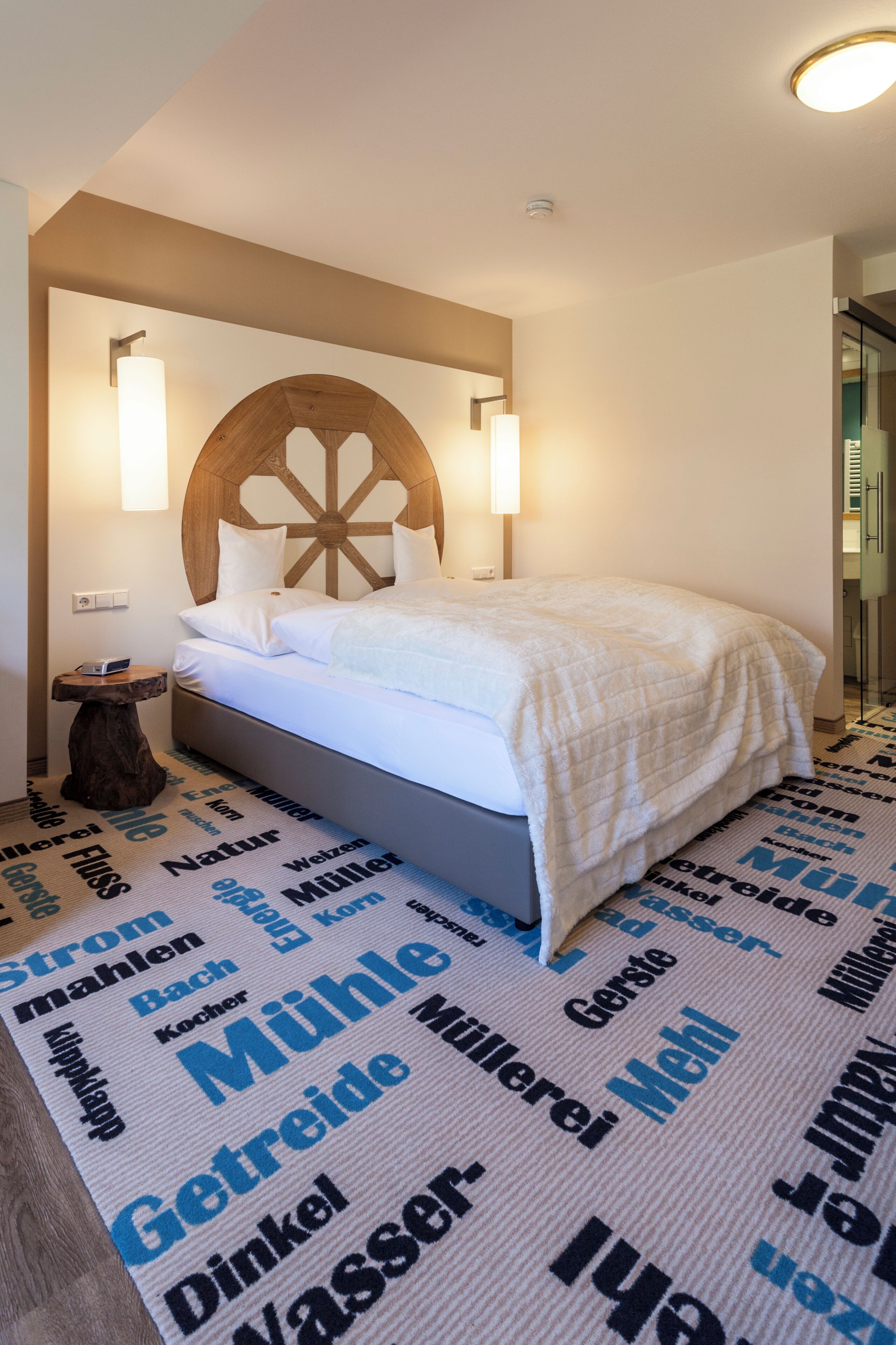 A hotel room with a bed, a wooden headboard, two bedside tables, and a wall with illuminated text.
