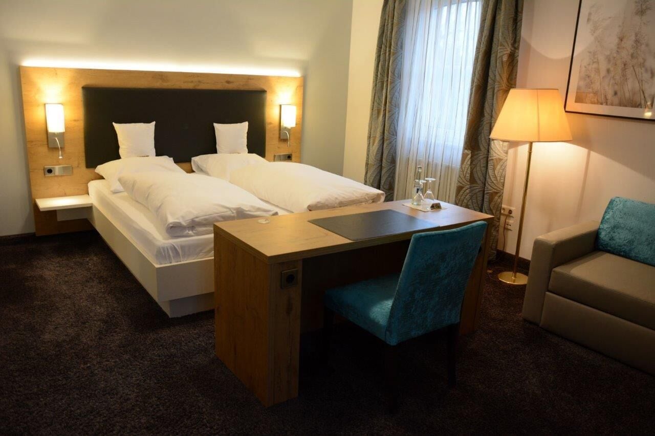 Ein Hotelzimmer mit Doppelbett, Schreibtisch, Stuhl, Nachttisch, Lampe und einer Sitzecke.