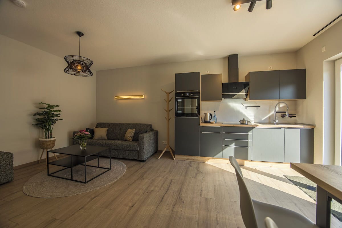 A modern kitchen with grey cabinets, a built-in oven, and a dining area with a wooden table and chairs.