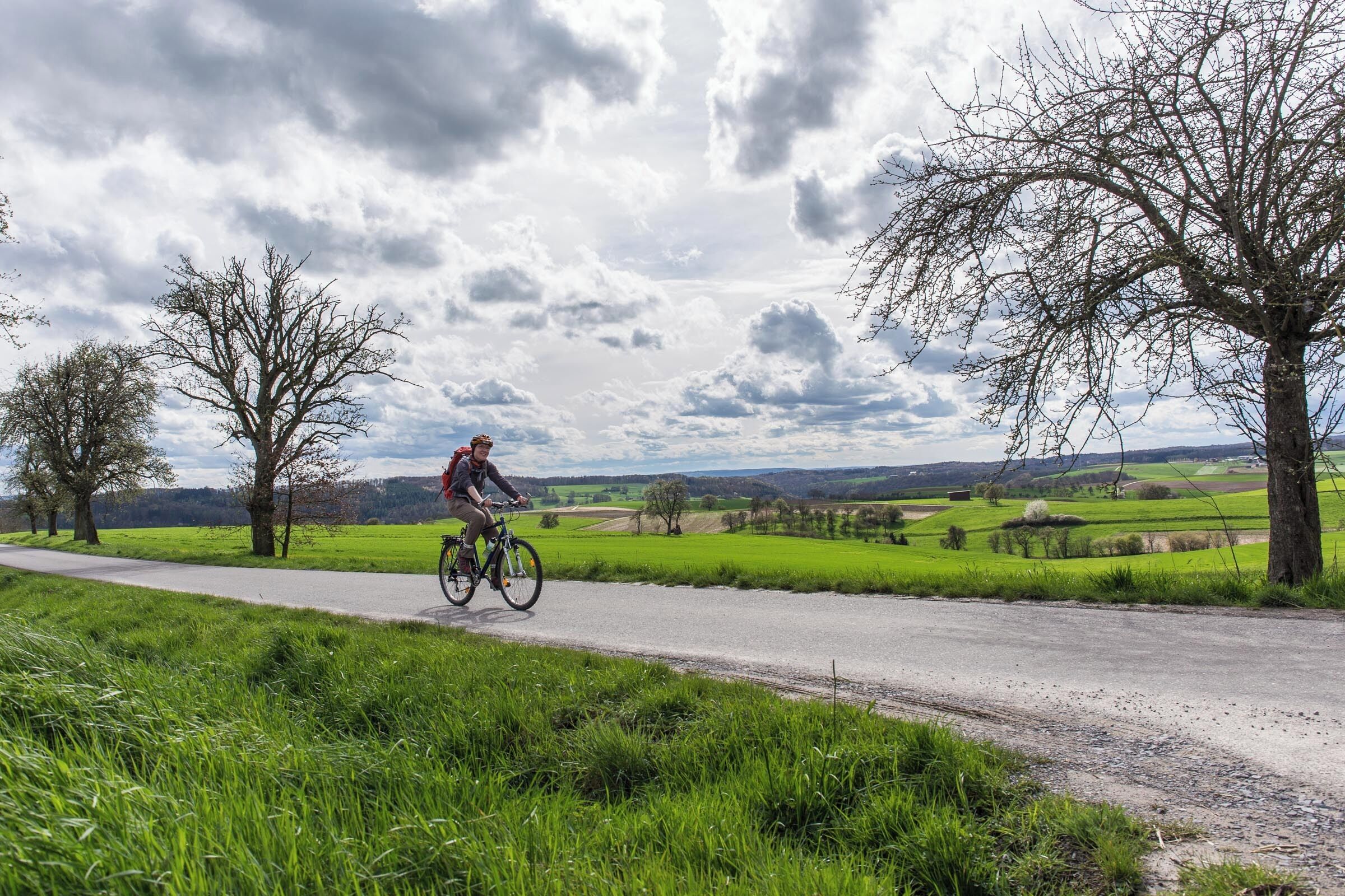 A cyclist on a paved path with a rural landscape in the background.