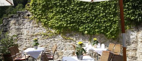 Un espacio para comer al aire libre con sillas de mimbre, manteles blancos y plantas en macetas.