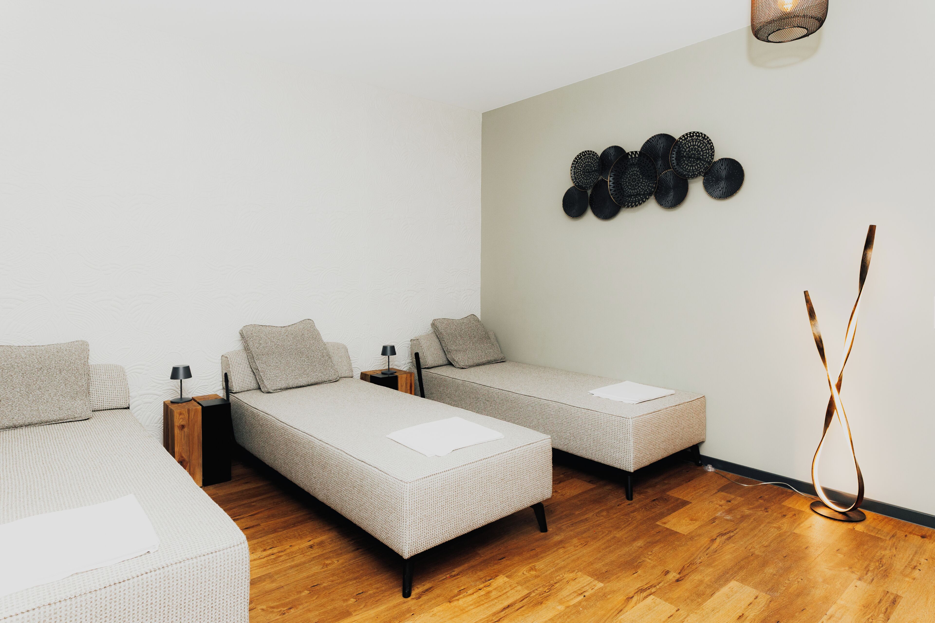 Una habitación moderna con dos camas individuales, una mesita pequeña, una lámpara de pared y una lámpara de pie.