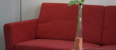 A red sofa, a glass table with a vase containing a single white flower, and a floor lamp.