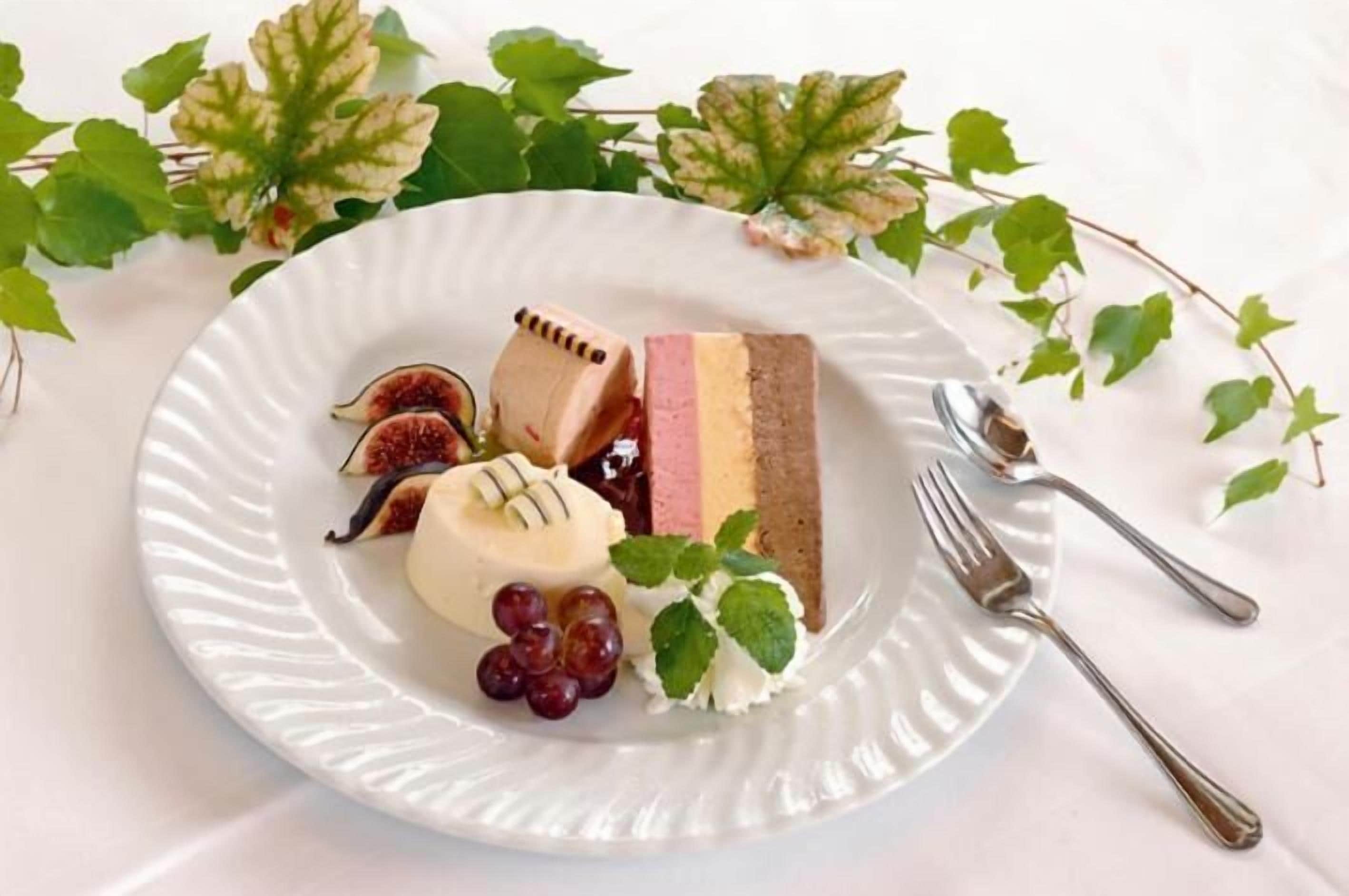 A plate with a slice of cake, figs, grapes, and whipped cream.