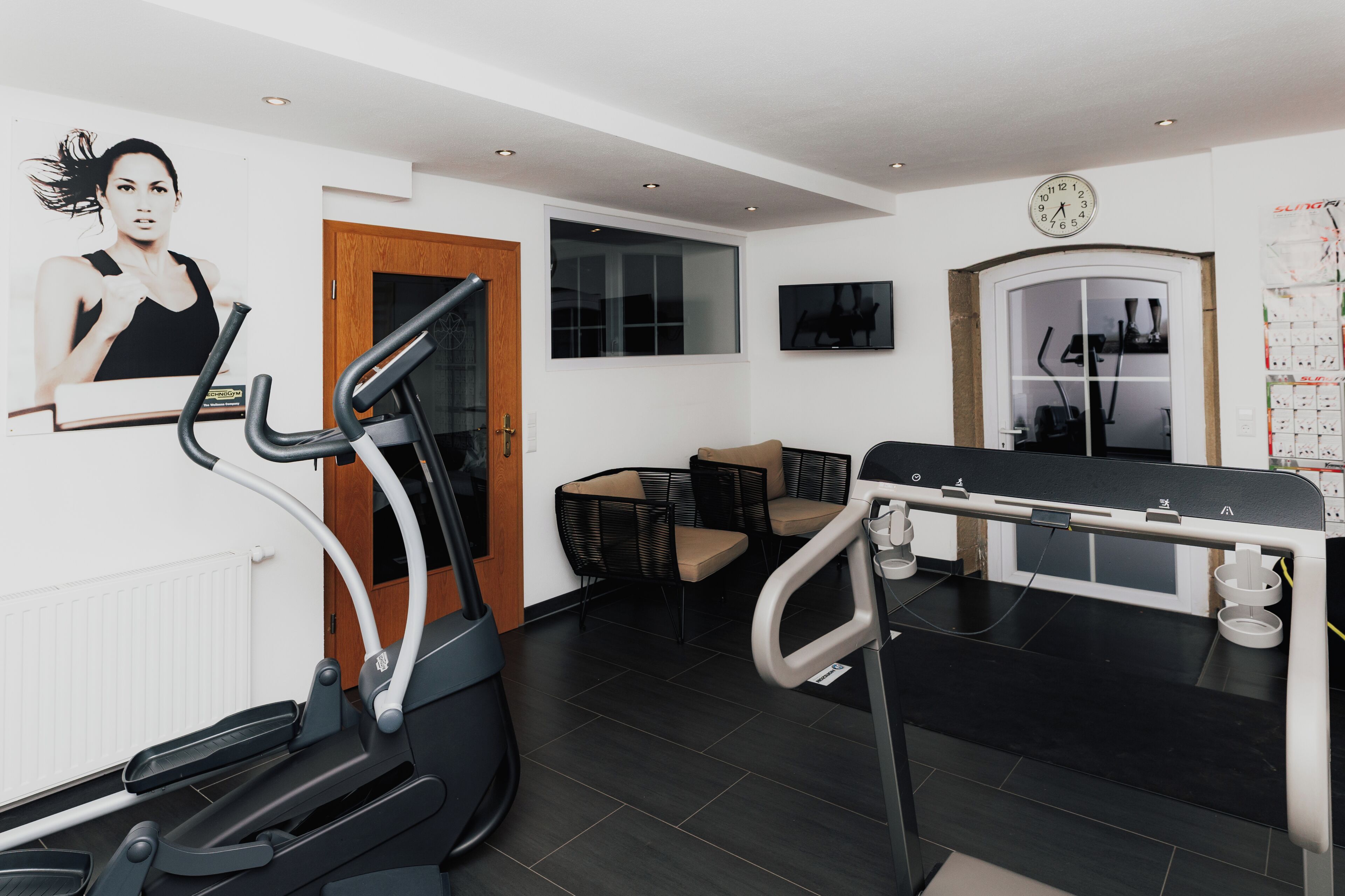 Un gimnasio en casa con equipo de ejercicio, un sofá y un reloj de pared.