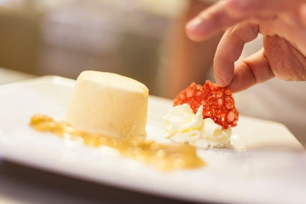 A dessert plate with a scoop of ice cream and a piece of red fruit on a white plate.