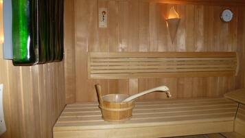 Een sauna met houten banken, een houten emmer met handvat, een wandlamp en een klok.