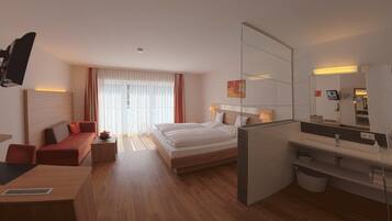 A modern hotel room with a bed, a desk, a sofa, a mirror, and a bathroom.