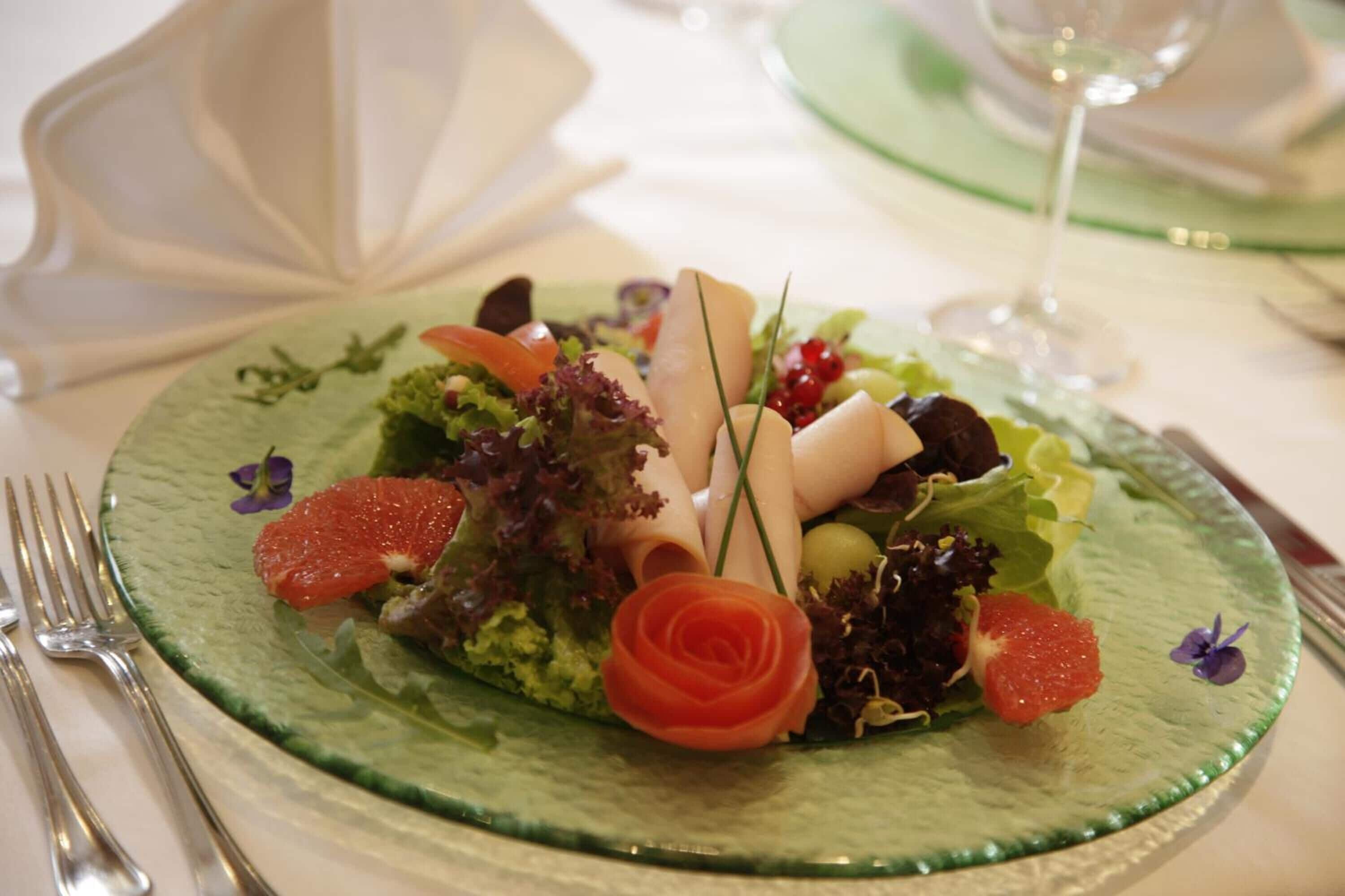 A green plate with a salad, a rose, and a glass of wine on a table.