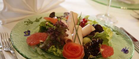 A green plate with a salad, a rose, and a glass of wine on a table.