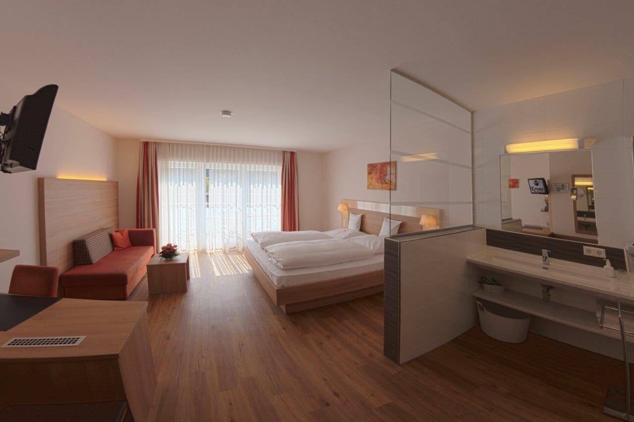 A modern hotel room with a bed, a desk, a sofa, a mirror, and a bathroom.