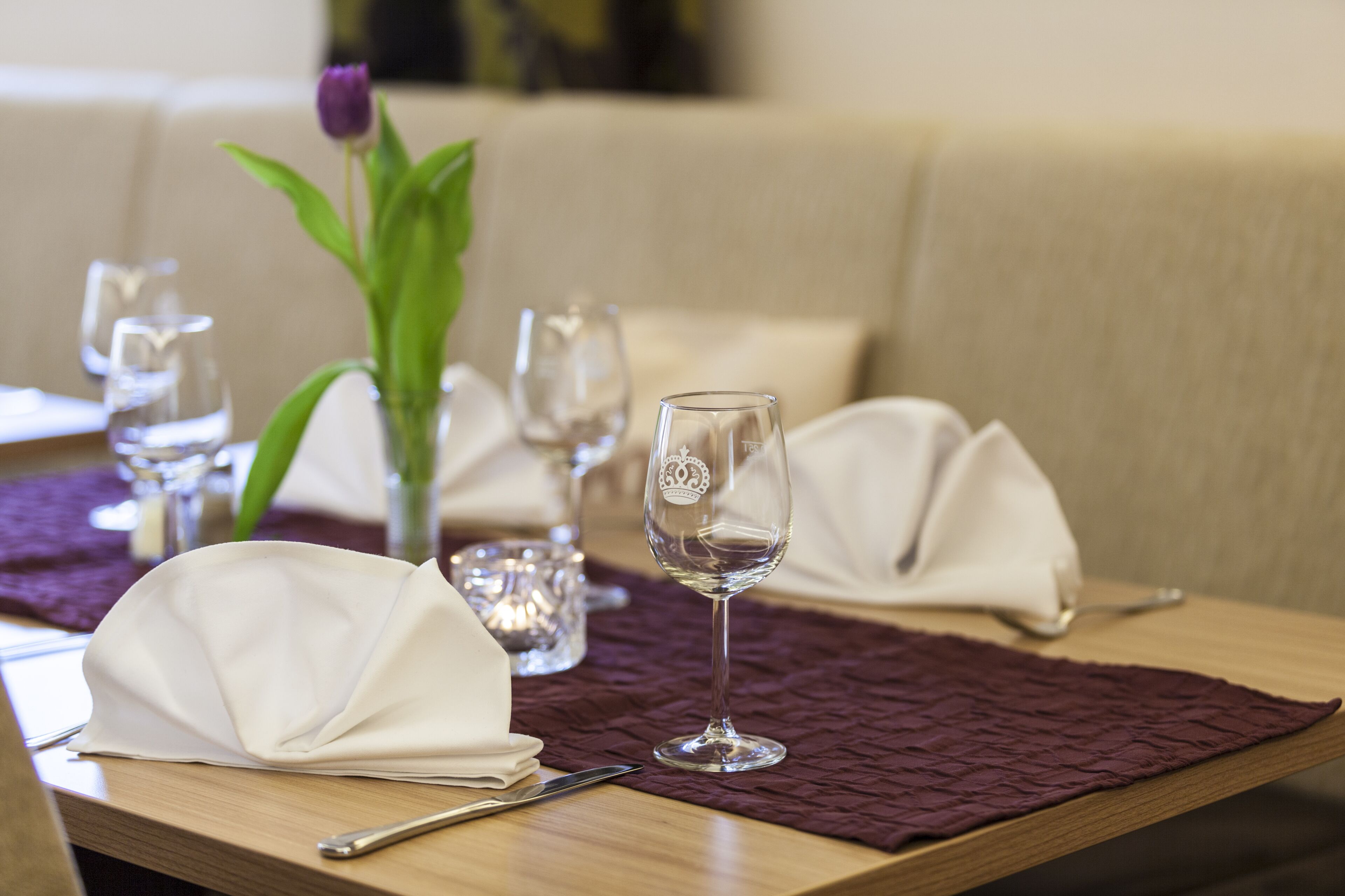 Una mesa de comedor dispuesta con servilletas blancas, una copa de cristal transparente y un camino de mesa morado.