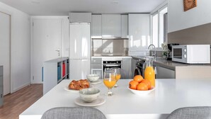 A modern kitchen with white cabinets, a built-in oven, a microwave, and a dining area with a table set for breakfast. - Lovely apartment WiFi, A/A, Parking, bike station, terrace & pool (Altea)