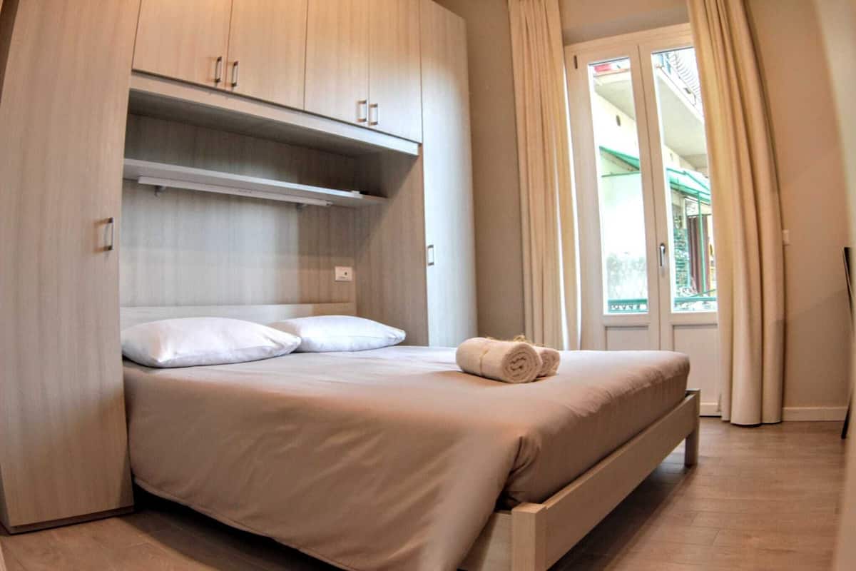 A bedroom with a bed, a wardrobe, and a view of the outside.
