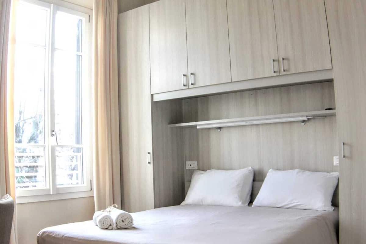 A bedroom with a bed, a window with curtains, and built-in wooden cabinets.