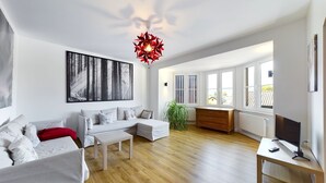 A modern living room with a sectional sofa, a wooden coffee table, a red pendant light, a large abstract painting, and a view of the outside through large windows. - Fantastic central Zugspitze view with parking lot  (Garmisch-Partenkirchen)