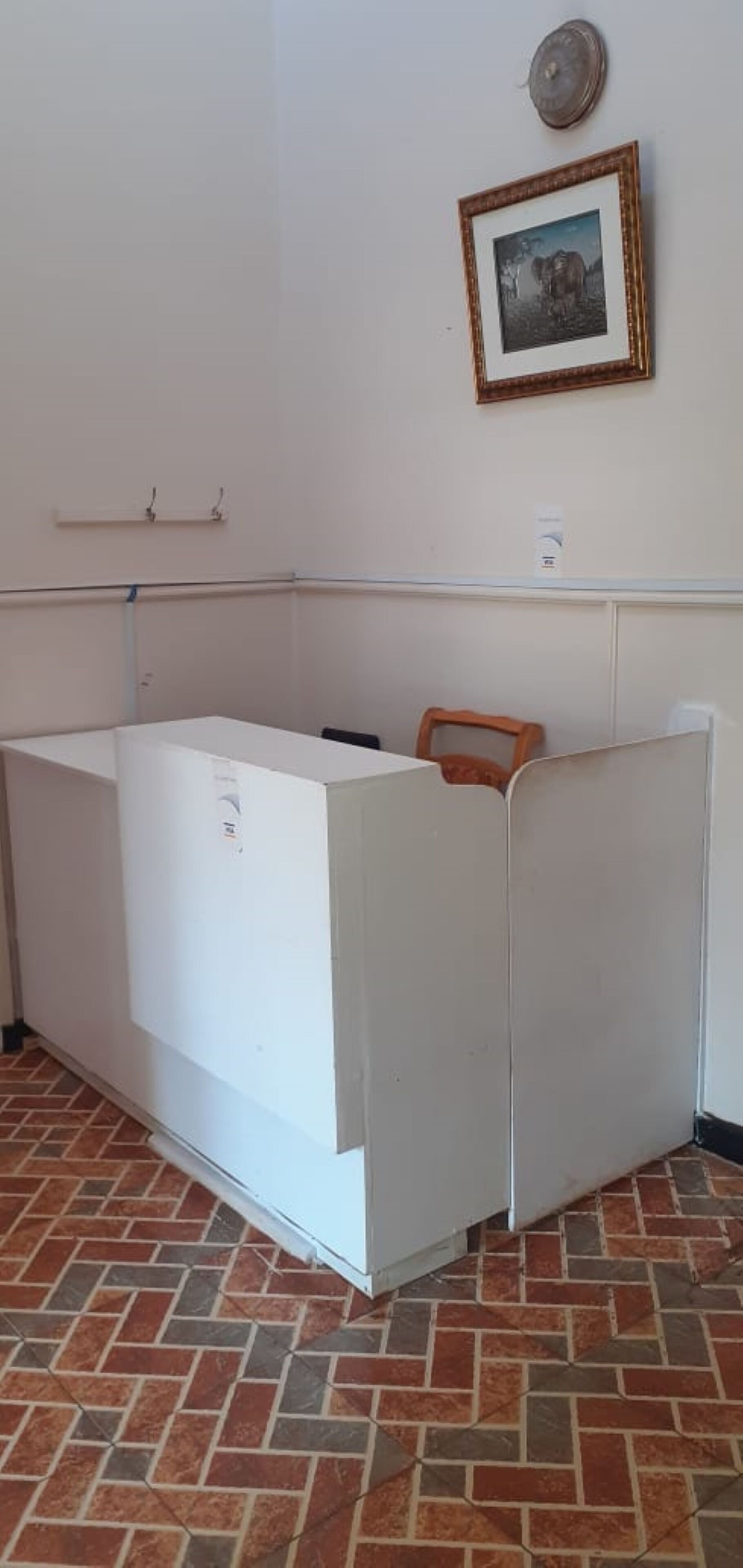 Una stanza con una scrivania bianca, una sedia, un quadro appeso e un pavimento piastrellato.