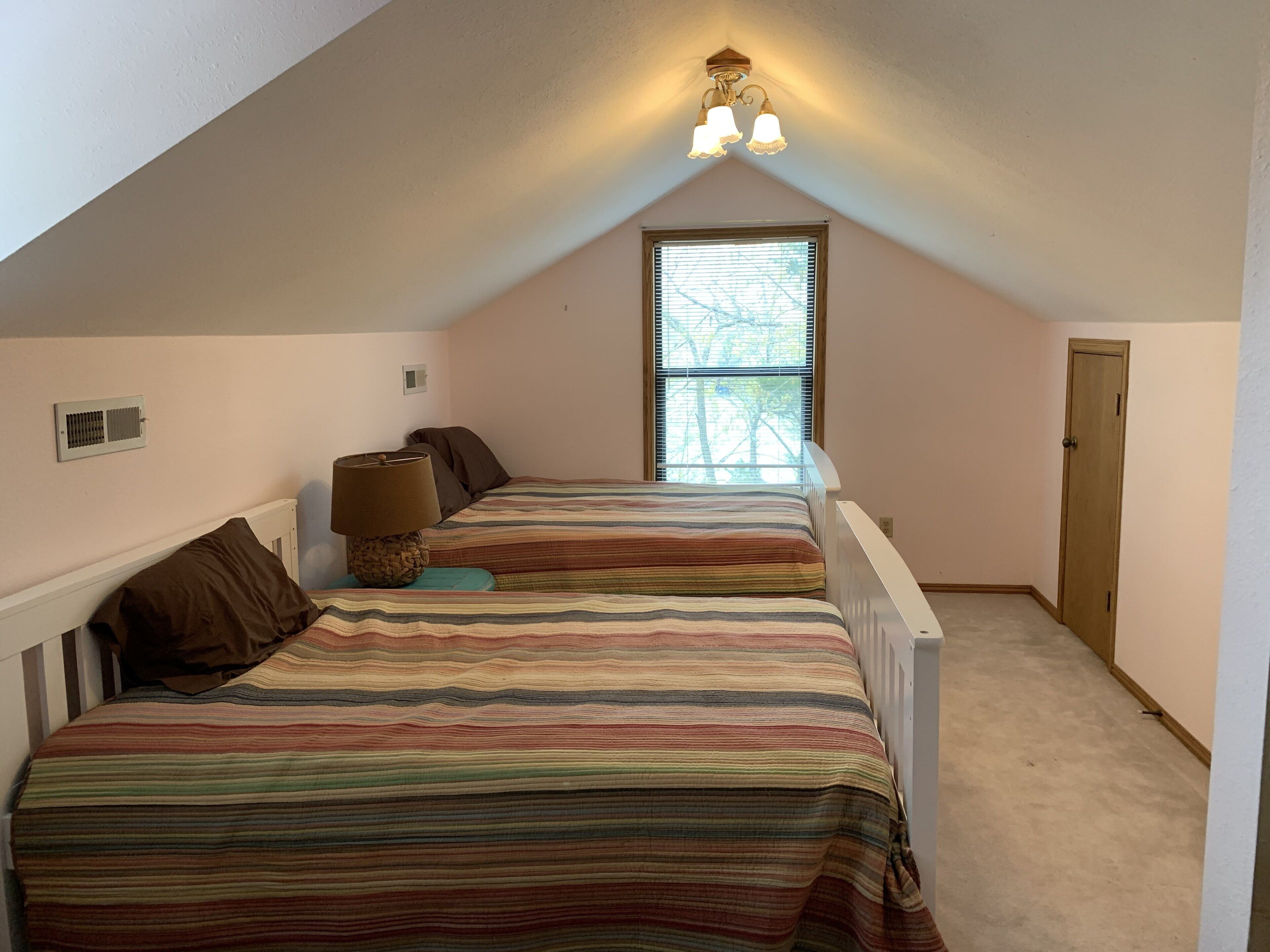 Un dormitorio con dos camas, una ventana, una puerta y una lámpara en el techo.