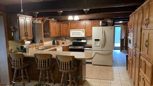 A kitchen with wooden cabinets, a central island with bar stools, a refrigerator, and a microwave.