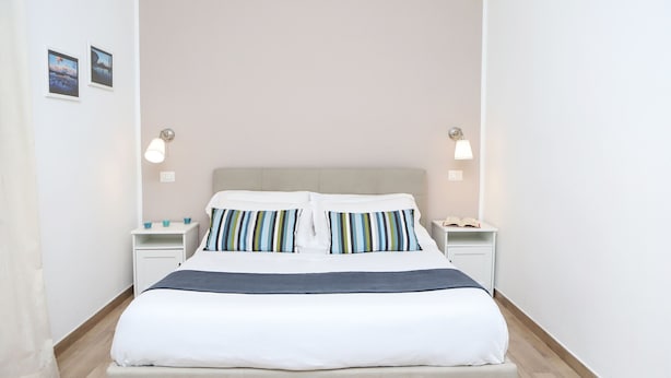 Una cama bien hecha con almohadillas a rayas, una mesita de noche con lámpara y un tocador con teléfono.
