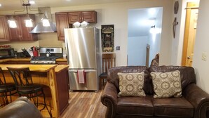 A modern kitchen with stainless steel appliances, a wooden dining area, and a brown leather sofa with patterned cushions.