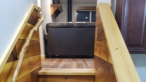 A wooden staircase leading to a dark-colored sofa in a room with wooden walls and a window.