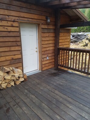 A wooden cabin with a door, a porch with a railing, and a stack of firewood.