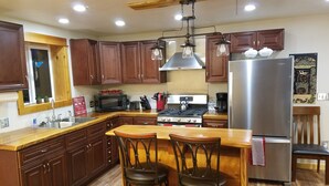 A kitchen with wooden cabinets, a stainless steel refrigerator, a gas stove, and a bar area with two stools.