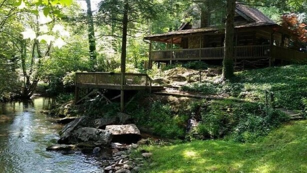 Eine rustikale Holzhütte mit einer Holzterrasse, umgeben von einem Wald und einem Bach.