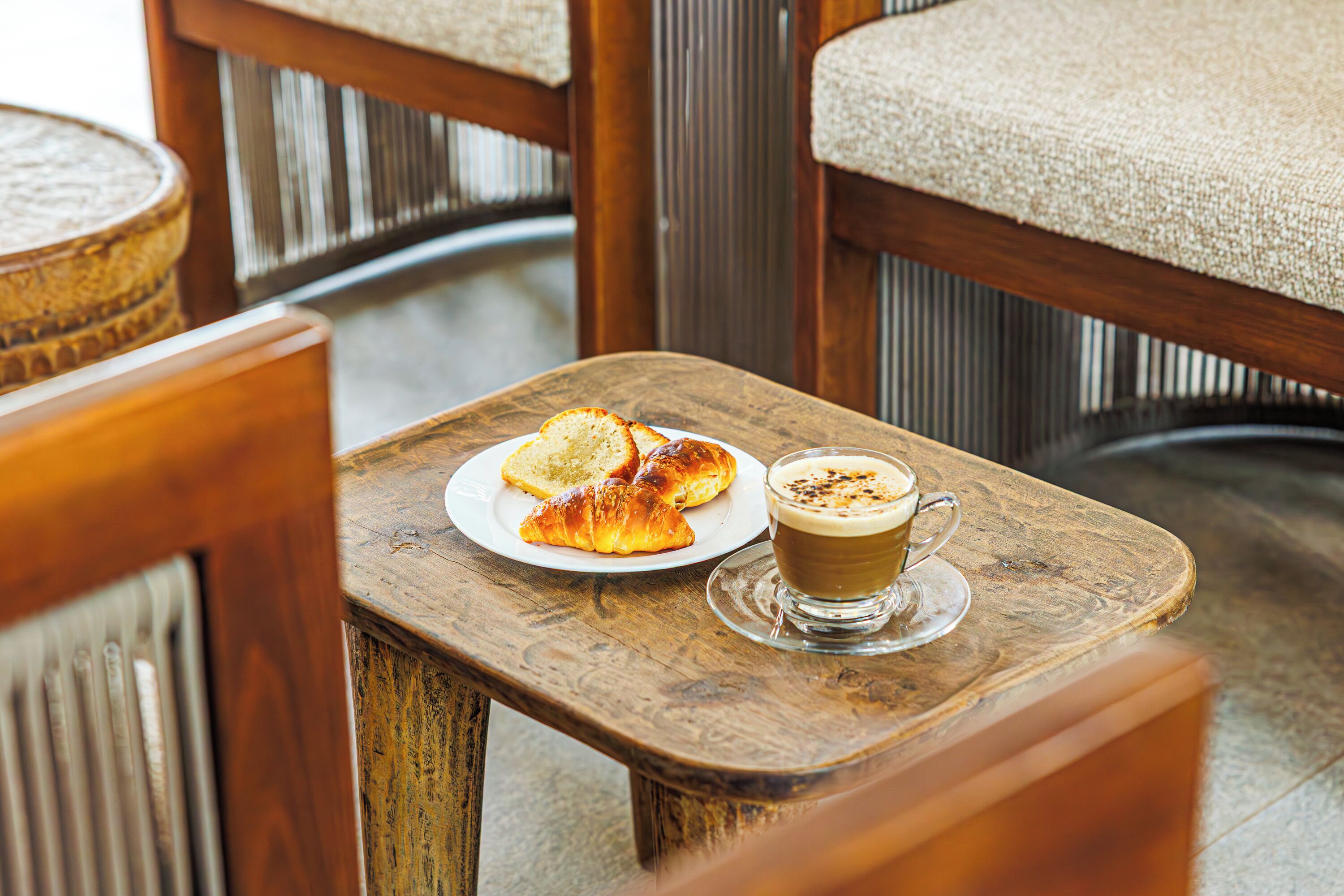 Una mesa de madera con un plato de cruasanes y una taza de café.