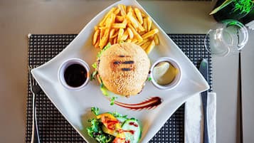 A square plate with a burger, fries, and a salad, accompanied by two sauces and a napkin.