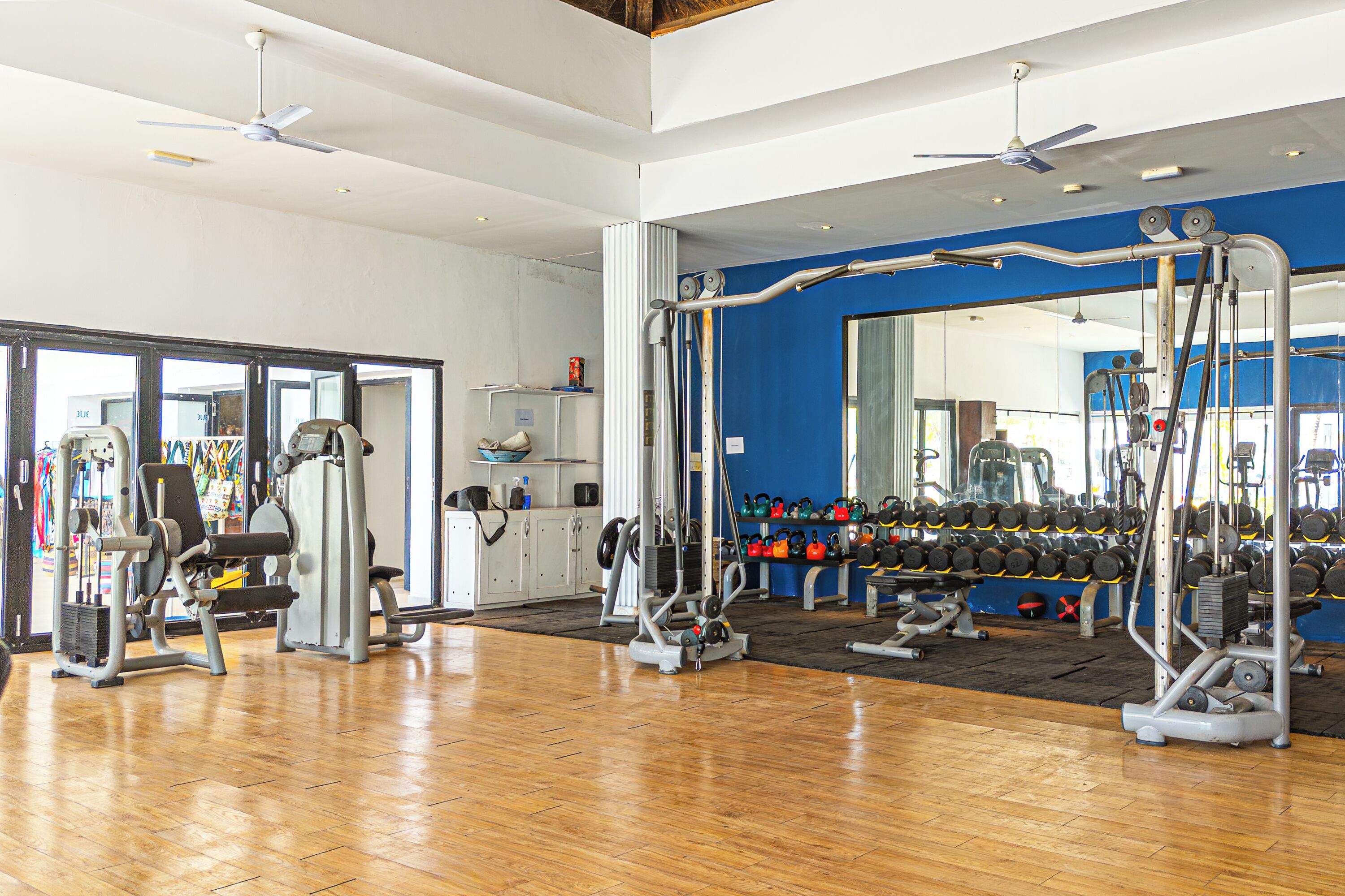 A gym with various exercise machines, weights, and a wooden floor.