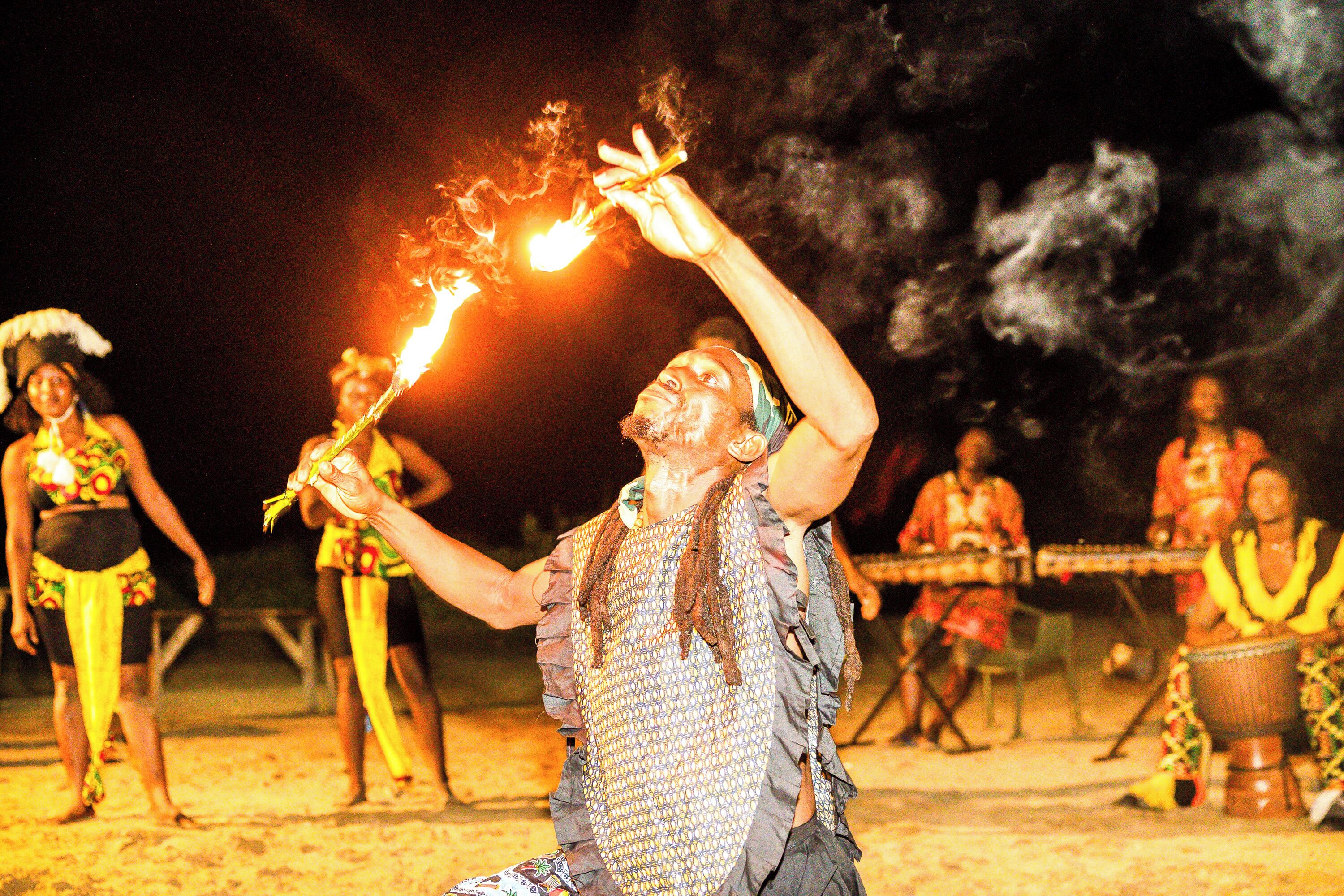 Una persona que actúa con antorchas de fuego, rodeada de otras personas vestidas con trajes tradicionales.