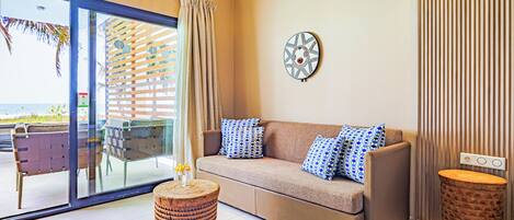 A modern living room with a sofa, two side tables, a decorative wall piece, and a view through a glass door to the outside.